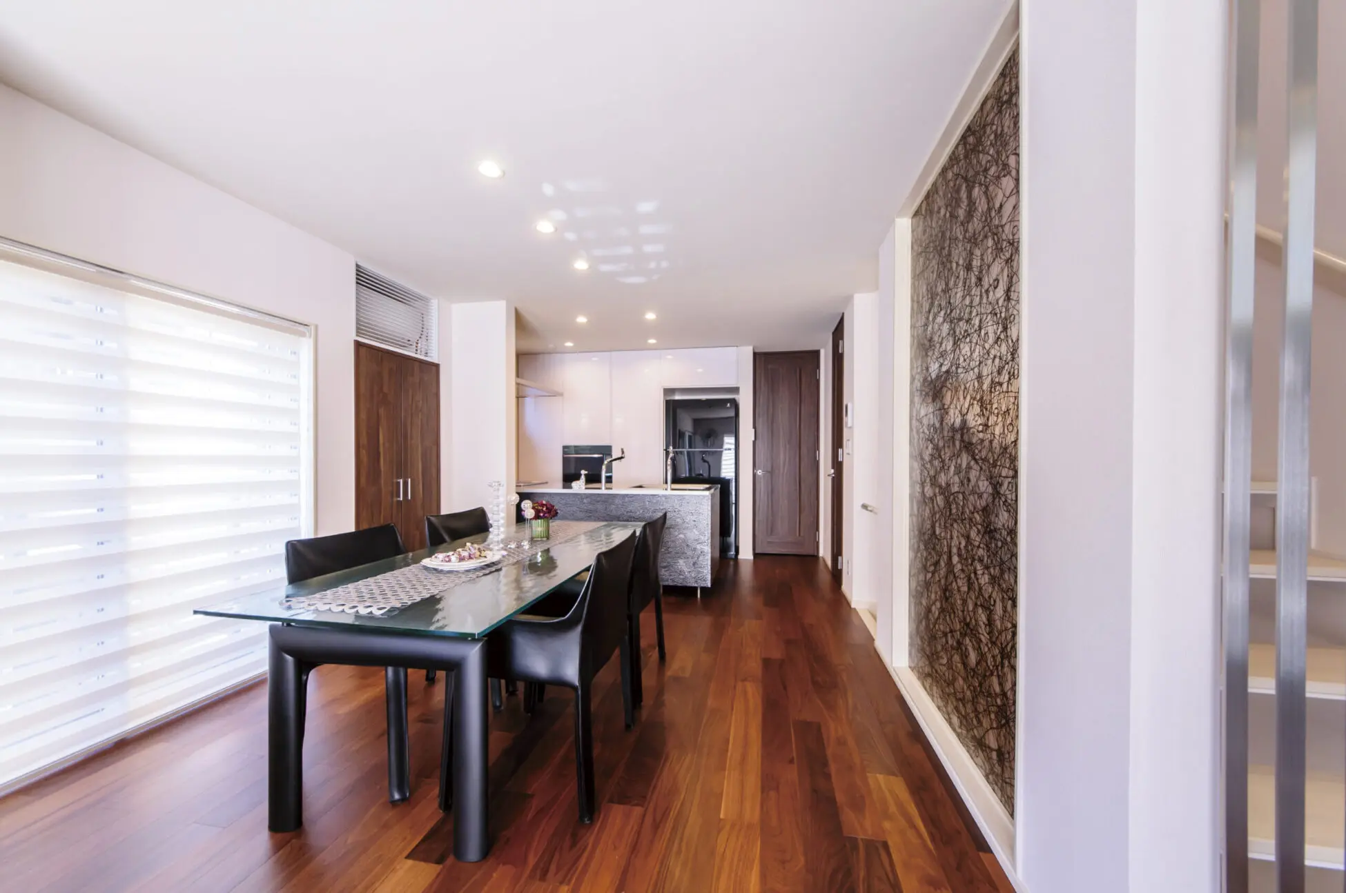 モダンで明るいダイニングルーム。茶色のフローリング、ガラスのテーブル、ダークカラーの家具が調和している。