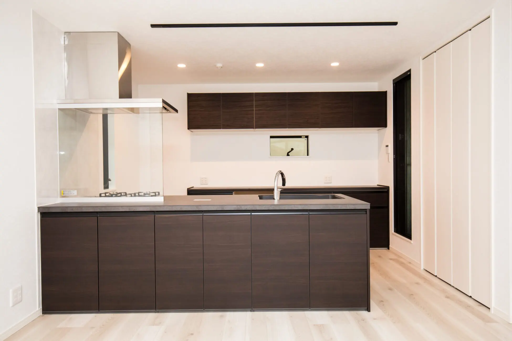 白い空間にダークな面材のキッチンが際立つ